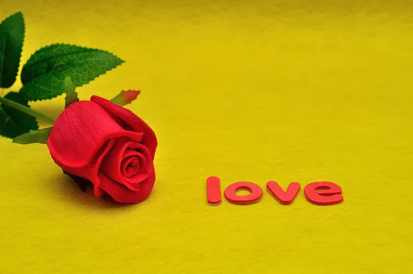 Het woord liefde en een rode roos tegen een gele achtergrond — Stockfoto