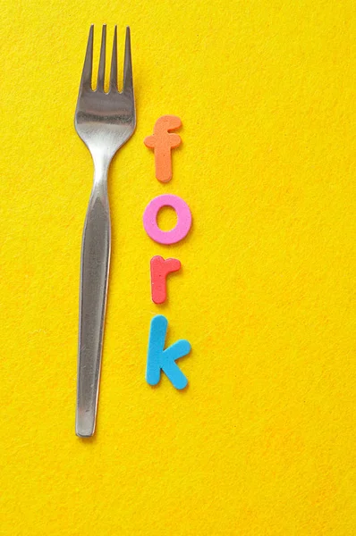 La palabra tenedor se muestra con un tenedor sobre un fondo amarillo — Foto de Stock