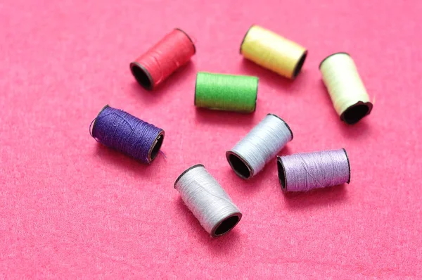 Pequenos rolos de linha de costura exibidos em um fundo rosa — Fotografia de Stock
