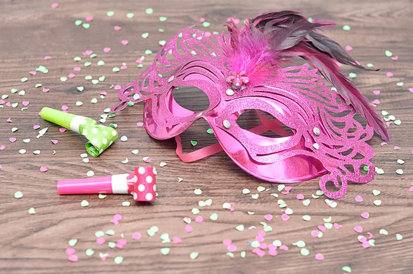 A pink masquerade mask with blowers and confetti