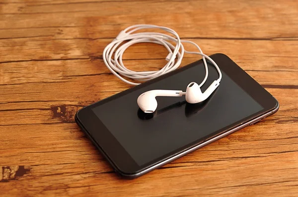 Białe słuchawki z telefon na drewnianym stole — Zdjęcie stockowe
