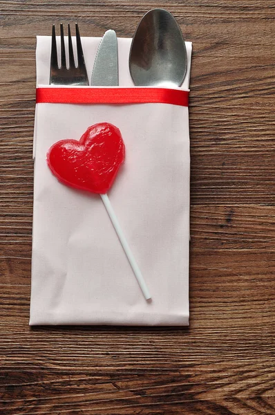 Cubertería exhibida en una servilleta blanca con una piruleta roja en forma de corazón — Foto de Stock