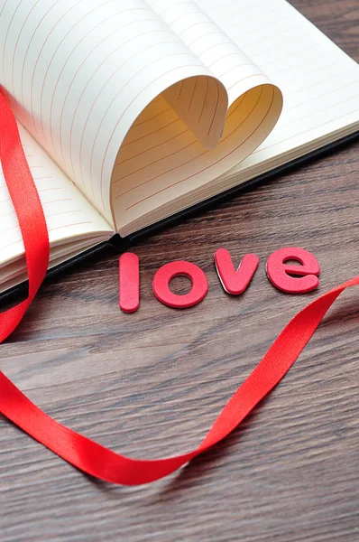 Pages of a book bend in a heart shape displayed with a red ribbon and the word love