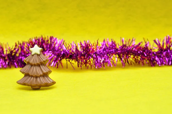黄色の背景にティンセルを持つチョコレートのクリスマス ツリー図形 — ストック写真