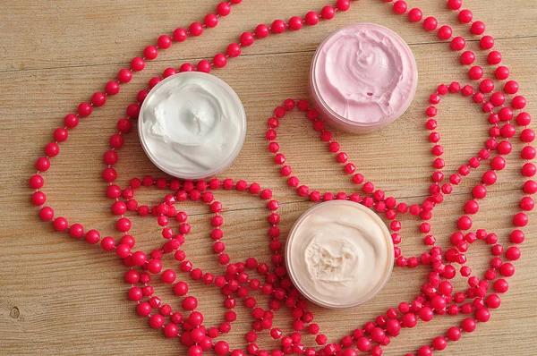 Three jars of body lotion displayed with strings of pink beads