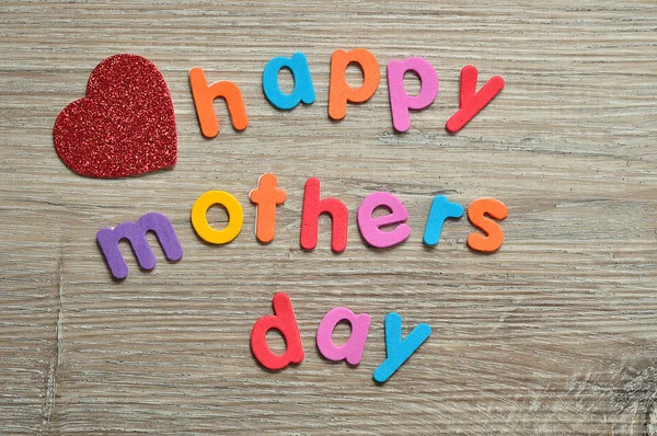 快乐的母亲节在一个红色的心在一个木质的背景五颜六色的字母 — 图库照片