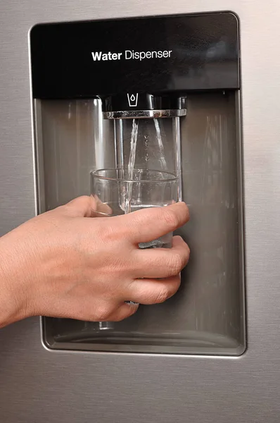 Une main de femme tenant un verre et de l'eau s'y versant d'un distributeur d'eau — Photo