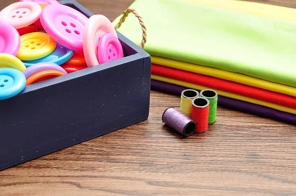 Un contenedor azul lleno de botones, rollos de hilo y una pila de material colorido — Foto de Stock