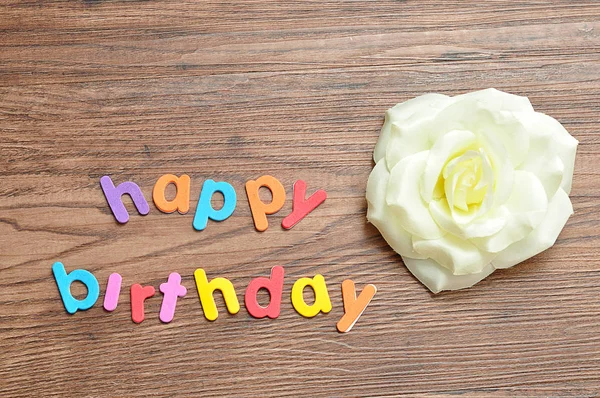 Happy birthday in colorful letters displayed with an artificial white rose