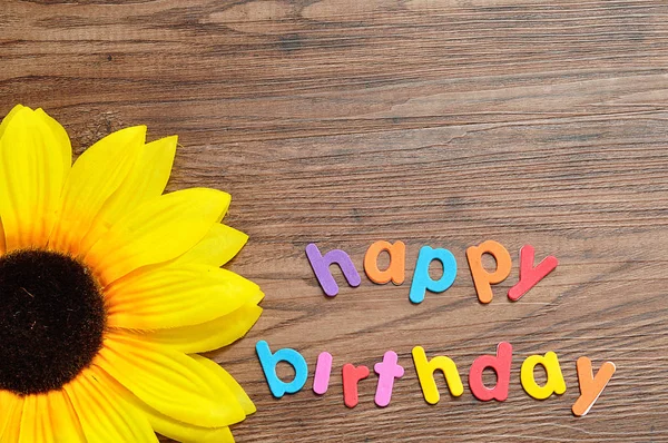 Happy birthday in colorful letters displayed with an artificial sunflower