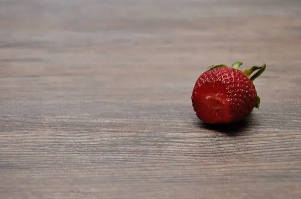A strawberry with a bite out on a wooden background — Stock Photo, Image