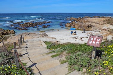 PACIFIC GROVE, CALIFORNIA - MARCH 17 2017: Stairway, entrance sign and people enjoying the surf, rocks and sand of the park at Asilomar State Beach on the Monterey Peninsula.