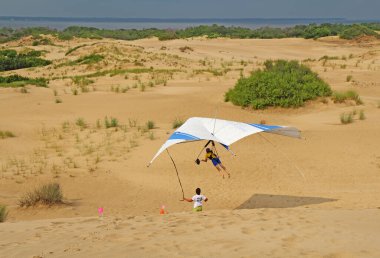 NAGS HEAD, NORTH CAROLINA - 29 Temmuz 2013: Öğrenci, Kitty Hawk Uçurtmaları Asma Okulu 'ndan bir eğitmenle Jockeys Ridge Eyalet Parkı' nın dış kıyılarındaki kum tepelerinin üzerinden uçuyor
