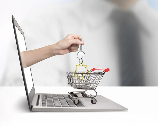 Hand from laptop screen taking house key in shopping cart — Stock Photo, Image