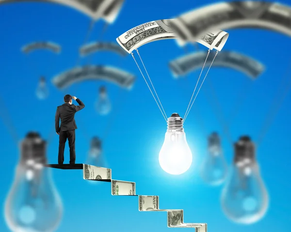 Mann auf Geldtreppe sucht Glühbirne mit Geld-Fallschirm — Stockfoto