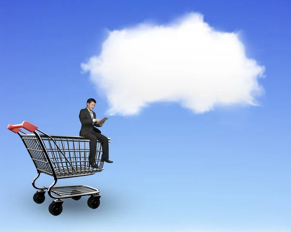 Man using tablet sitting on shopping cart with white cloud — Stock Photo, Image