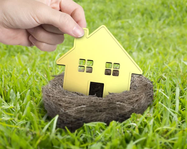 Woman hand holding golden house in nest — Stock Photo, Image