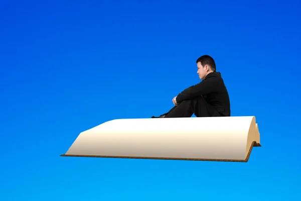 Muž sedí na knihy létání na modré obloze — Stock fotografie