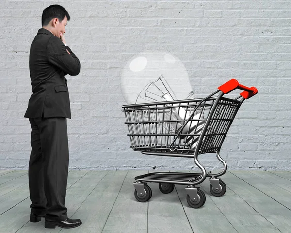 Standing man looking at shopping cart with large light bulb — Stock Photo, Image