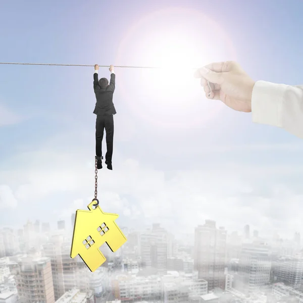 Businessman shackled by gold house hanging on rope — Stock Photo, Image