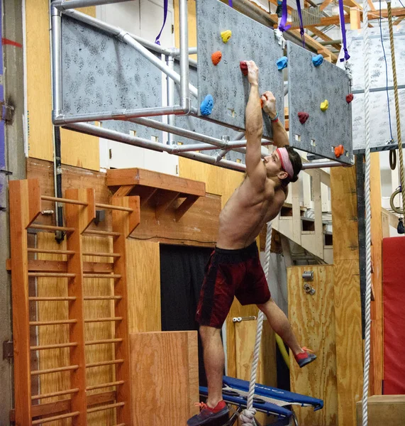 Joven atleta masculino, Adam Rahl, cuelga de un muro de escalada flotante durante una competición de guerreros ninja celebrada en Albuquerque, Nuevo México, en enero de 2017. Aunque parece derrotado, pasó a completar este obstáculo — Foto de Stock