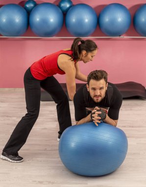 Koçunun spor salonunda spor topuyla esneme egzersizleri yapmasına yardım eden genç bir adam.. 