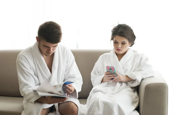 有吸引力的年轻夫妇正在看智能手机和杂志 — 图库照片