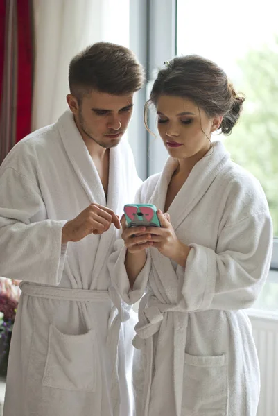 有吸引力的年轻夫妇正在看在酒店房间里的智能手机 — 图库照片