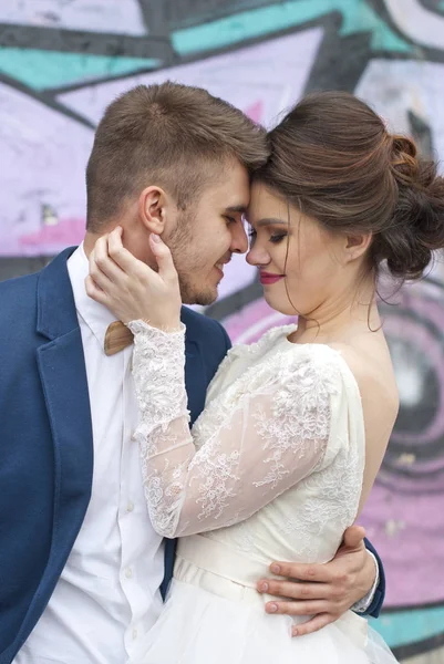 Απλά Έγγαμος αγάπη hipster ζευγάρι σε γάμο φόρεμα και κουστούμι εξωτερική σε περιβάλλον πόλης πολύχρωμα γκράφιτι τοίχο. Ευτυχισμένη νύφη και τον γαμπρό περπάτημα τρέξιμο και χορό. Ρομαντικό παντρεμένη νεαρή οικογένεια. — Φωτογραφία Αρχείου