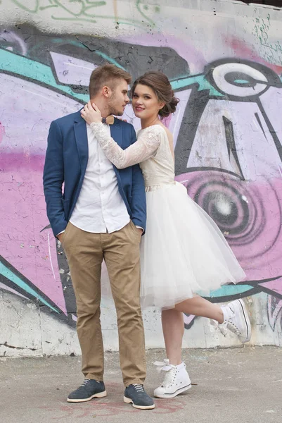 Just married loving hipster couple in wedding dress and suit outdoor in city setting against colorful graffiti wall. Happy bride and groom walking running and dancing. Romantic Married young family. — Stock Photo, Image