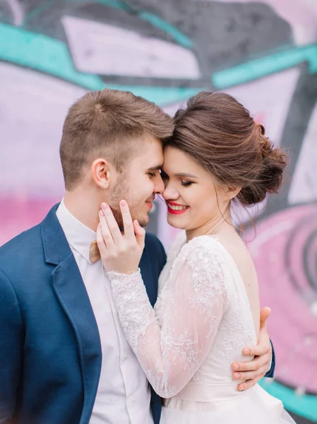 Just married loving hipster couple in wedding dress and suit outdoor in city setting against colorful graffiti wall. Happy bride and groom. Romantic Married young family. — Stock Photo, Image