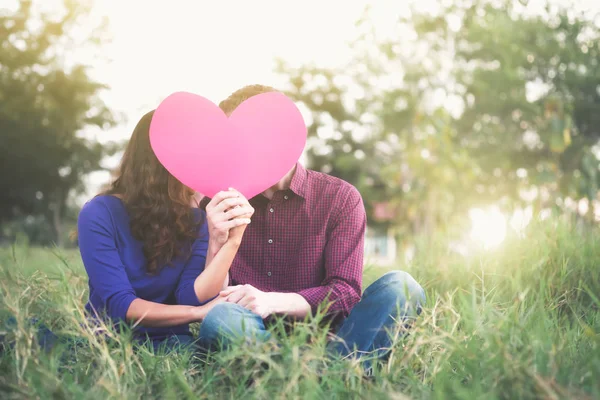 Joven pareja feliz enamorada sosteniendo el corazón de papel rojo en el jardín. Amor, Romance y San Valentín Concepto idea . — Foto de Stock