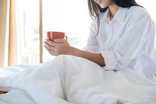 Relaxante jovem mulher desfrutando de seu café enquanto sentado na cama . — Fotografia de Stock