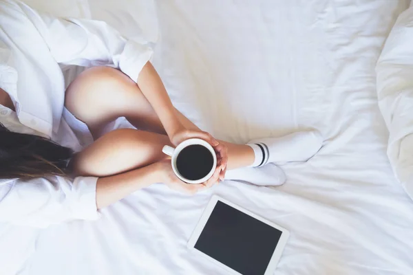 Relaxante jovem mulher desfrutando de seu café enquanto sentado na cama . — Fotografia de Stock