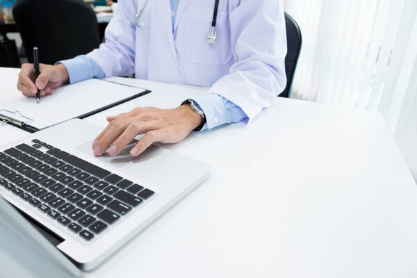 Doctor working with laptop computer and writing on paperwork