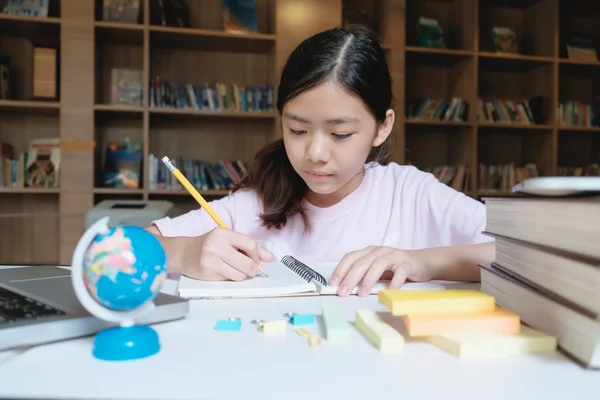 Chica leyendo y escribiendo en la biblioteca de la escuela . — Foto de Stock