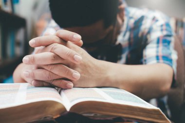 Man praying, hands clasped together on her Bible.  clipart