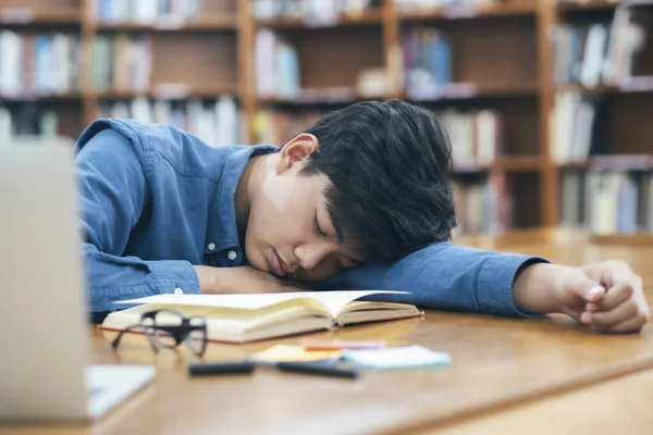 疲惫不堪的年轻学生躺在桌子上 在图书馆里翻开书 — 图库照片