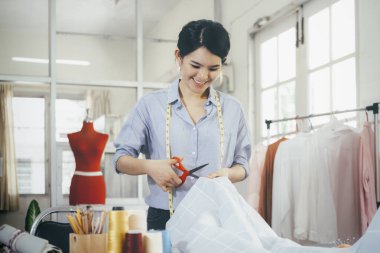 Stüdyoda çalışan genç bayan moda tasarımcısı yeni koleksiyon giysileri tasarlıyor. Robot resimde terzi kumaşı kesiyor..