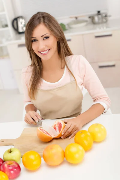 Woman cutting grapefruit in kitchen — Stock Photo, Image
