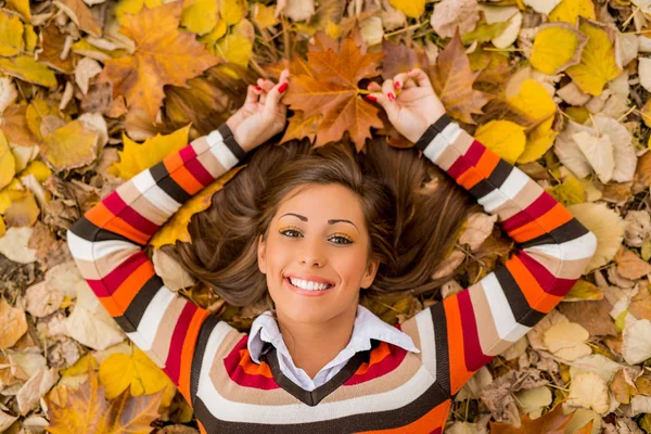 Sonriente mujer acostada en el follaje de otoño — Foto de Stock