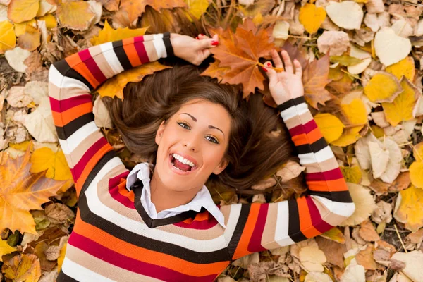 Sonriente mujer acostada en el follaje de otoño — Foto de Stock