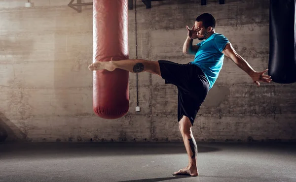 Poinçonnage homme avec sac de boxe jambe — Photo