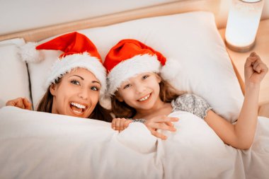 Genç anne battaniye ile örtülü kızıyla birlikte Noel arifesi, Noel Baba için bekliyor yatakta zevk.