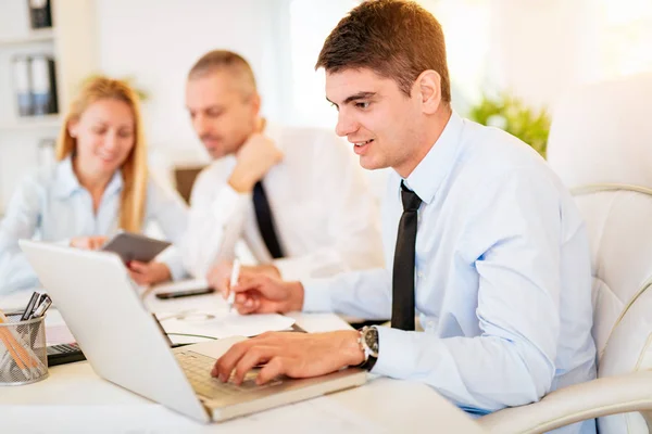 Joven Hombre Negocios Guapo Sonriente Trabajando Portátil Oficina Sus Colegas —  Fotos de Stock