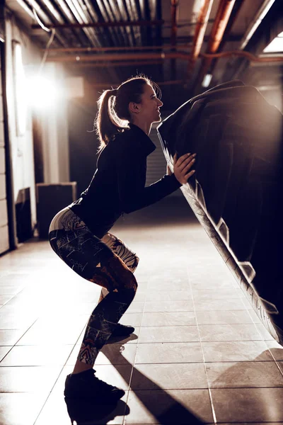 Jovem Mulher Muscular Lançando Pneu Cross Fit Formação Garagem — Fotografia de Stock