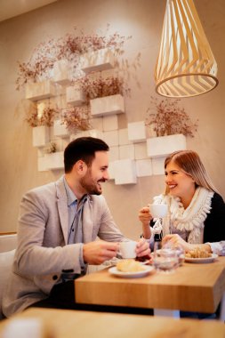 Genç adam ve genç kadın kafede oturan ve gülümseme ile konuşuyor. Onlar kahve içme ve having kahvaltı.