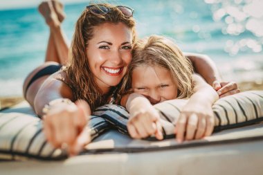 Sevimli küçük kız sahilde zevk güzel annesiyle. Onlar işaret ve kameraya seyir. 