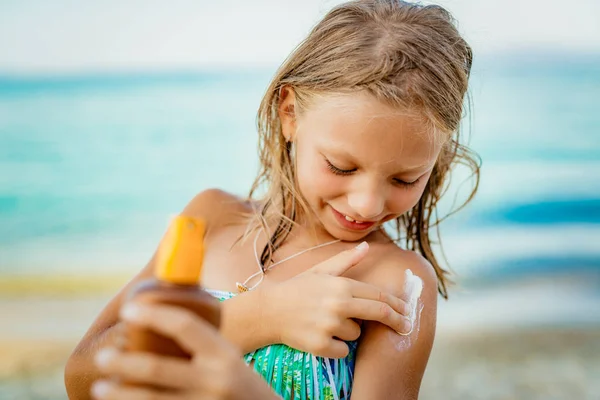 Carino Sorridente Bambina Che Applica Lozione Abbronzatura Sulla Spiaggia — Foto Stock