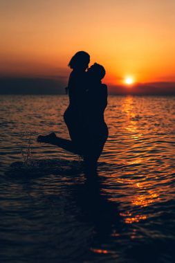 Sevgi dolu bir kaç sarılma ve gün batımında sahilde öpüşme silüeti.